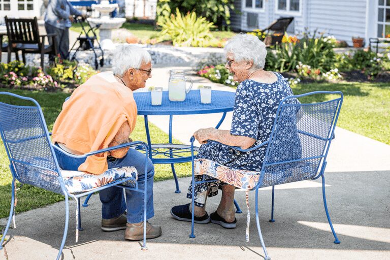 Two senior women drinking lemonade and chatting in a courtyard