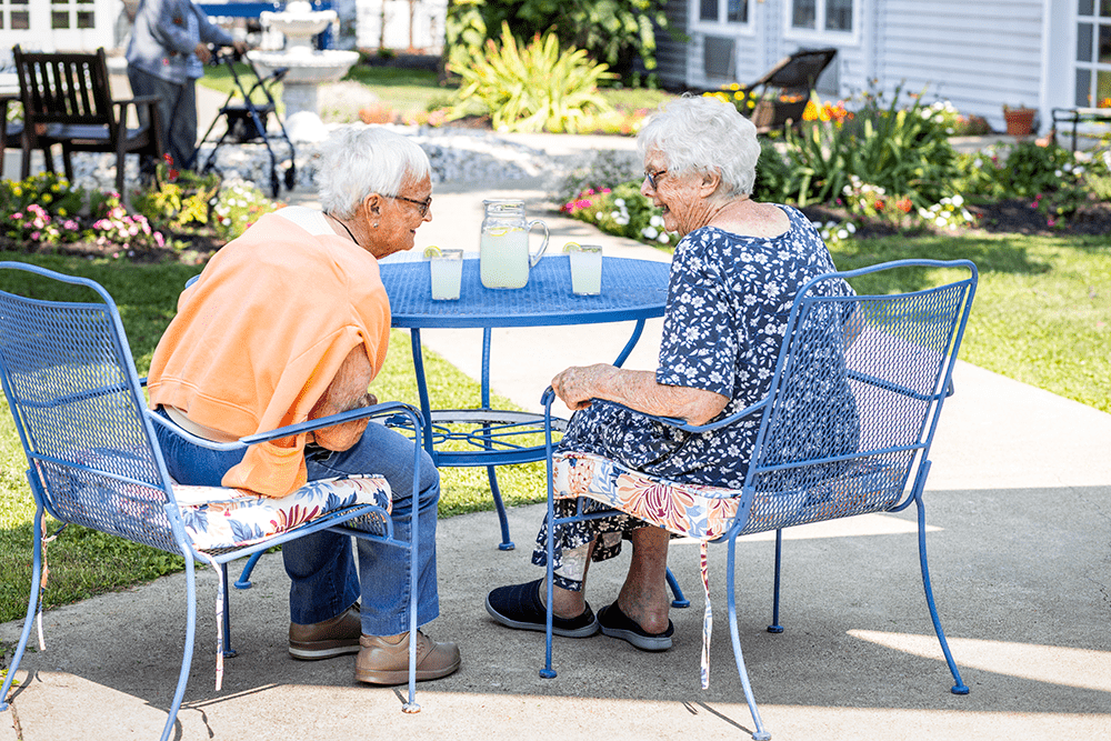 Two senior women drinking lemonade and chatting in a courtyard
