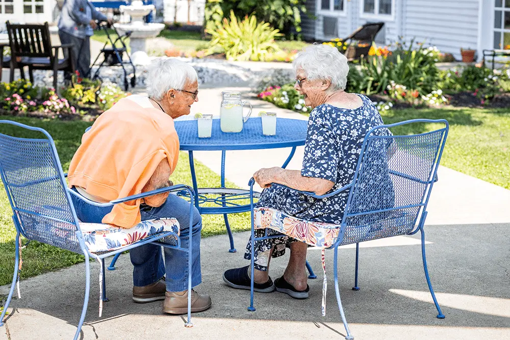 Two senior women drinking lemonade and chatting in a courtyard