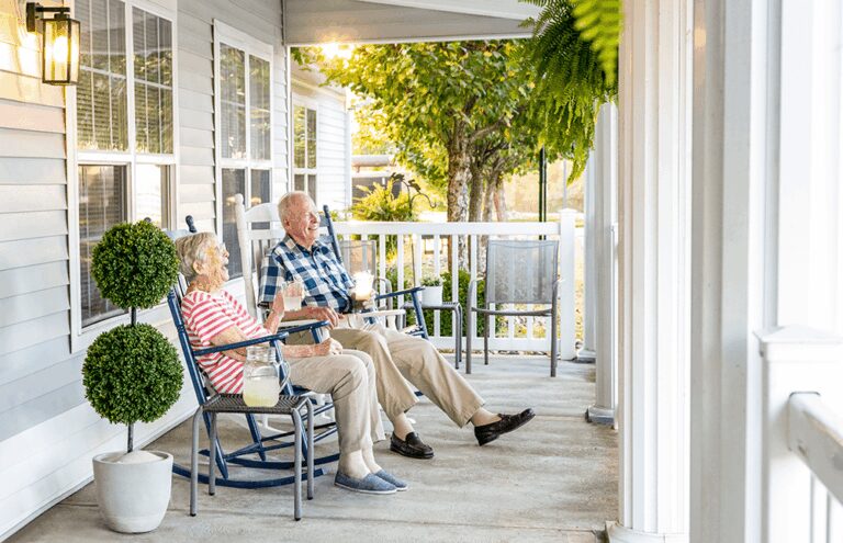 A senior man and woman sitting on the front porch drinking lemonade